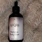 Uqlo Radiance Body Elixir bottle on a textured beige surface