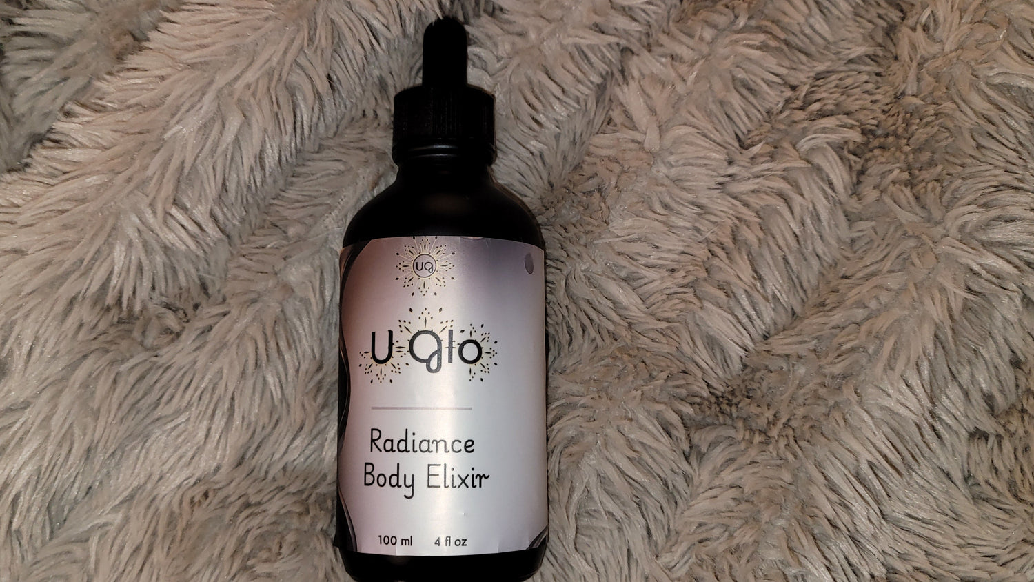 Uqlo Radiance Body Elixir bottle on a textured beige surface